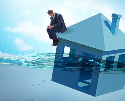 Ein Mann sitzt auf einem Haus, dass im Wasser schwimmt | Insolvenz Notverkauf Immobilie