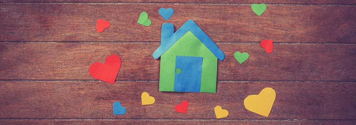 Ein buntes Haus aus Papier und bunte Herzen aus Papier liegen auf einem Holztisch | Valentinstag Immobilien Makler
