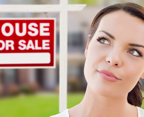 Frau überlegt vor einem Haus mit einem "Zu verkaufen"-Schild, wie sie im Alter wohnen möchte | Wohnen im Alter