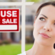 Frau überlegt vor einem Haus mit einem "Zu verkaufen"-Schild, wie sie im Alter wohnen möchte | Wohnen im Alter