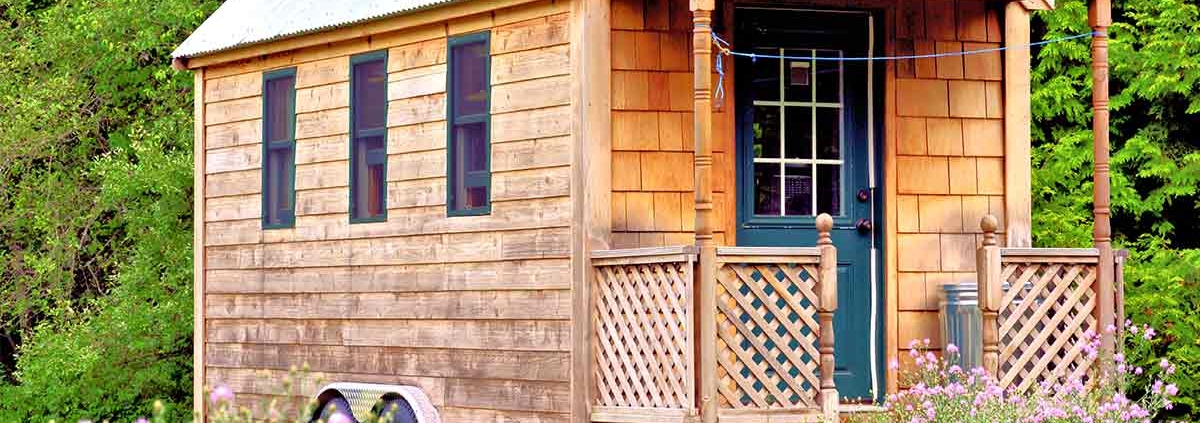 Ein Tiny House aus Holz steht auf einer Wiese.