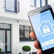 Eine Hand hält ein Smartphone mit einer Sicherheits-App vor einem Haus | Proptechs