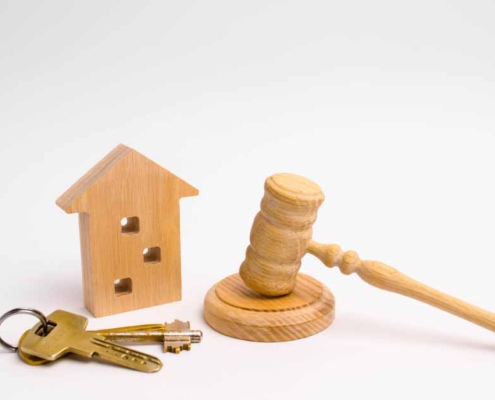 Ein Schlüsselbund, ein Häuschen aus Holz und ein Richterhammer liegen auf einer weißen Oberfläche - Immobilienverkauf